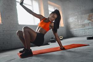 mooie jonge afrikaanse vrouw die op mat in de sportschool traint foto