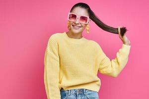 speelse jonge vrouw met een funky bril die haar lange haar vasthoudt en lacht tegen een gekleurde achtergrond foto