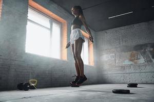 volledige lengte van mooie jonge vrouw die met touw in de sportschool springt foto