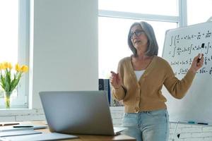 zelfverzekerde senior vrouw die whiteboard wijst terwijl ze in de klas staat foto