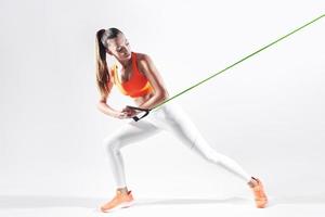 zelfverzekerde jonge vrouw die weerstandsband gebruikt tijdens het sporten tegen een witte achtergrond foto