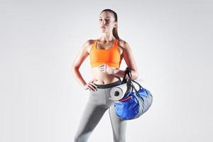 zelfverzekerde jonge vrouw in sportkleding die een tas draagt tegen een witte achtergrond foto