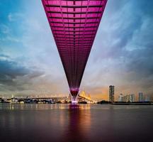 paars led-licht onder de brug over de rivier op een bewolkte dag in de lucht. bhumibol-brug, samut prakan, thailand foto