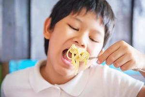 jongen eet heerlijke roomsaus spaghetti - Italiaans eten met mensen concept foto