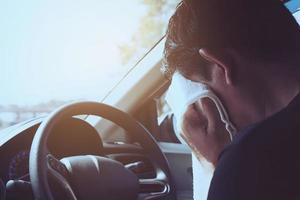 vermoeide man die zijn gezicht afveegt met een witte koude verfrissingsdoek tijdens het autorijden - lange reis rijden met een vermoeid concept foto