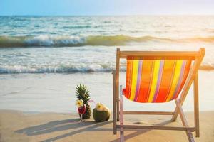 relax strandstoel met kokos ananas en cocktailglas op schoon zandstrand met blauwe zee en heldere hemel - zee natuur achtergrond ontspannen concept foto