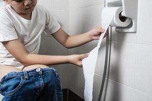 Aziatische jongen zittend op toiletpot met papieren zakdoekje - gezondheidsprobleem concept foto