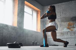 volledige lengte van jonge Afrikaanse vrouw die traint met elastische weerstandsband in de sportschool foto