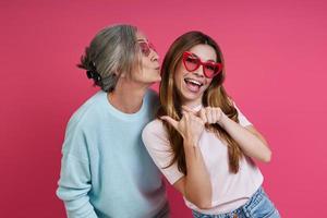 speelse moeder en volwassen dochter in funky brillen die plezier hebben tegen roze achtergrond foto