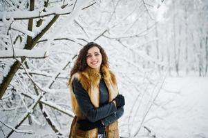 elegantie krullend meisje in bontjas in besneeuwde forest park in de winter. foto