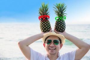 mooie paar verse ananas die jongens- en meisjesbril in toeristische handen zet met zeegolfachtergrond - gelukkig plezier met gezond vakantieconcept foto