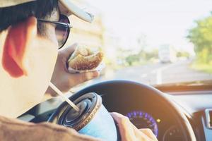 man eet gevaarlijk hotdog en koud drankje tijdens het autorijden foto