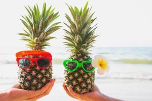 heerlijke verse paar ananassen die een bril in toeristische handen zetten met zeegolfachtergrond - gelukkige liefde en plezier met gezond vakantieconcept foto