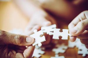 handen van een persoon klein kind en ouder spelen puzzelstukje samen op houten tafel thuis, concept voor vrije tijd met familie, spelen met de ontwikkeling van kinderen, onderwijs en plezier. foto