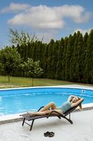 jonge vrouw liggend op een dek char bij het zwembad in de achtertuin van het huis