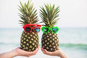 heerlijke verse paar ananassen die een bril in toeristische handen zetten met zeegolfachtergrond - gelukkige liefde en plezier met gezond vakantieconcept foto