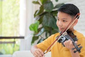 een klein Aziatisch kind speelt en oefent viool muzikaal snaarinstrument tegen in huis, concept van muzikaal onderwijs, inspiratie, tiener kunstacademie student. foto