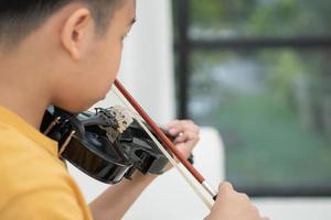 een klein Aziatisch kind speelt en oefent viool muzikaal snaarinstrument tegen in huis, concept van muzikaal onderwijs, inspiratie, tiener kunstacademie student. foto