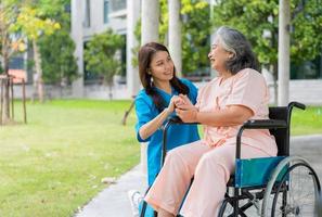 Aziatische zorgvuldige verzorger of verpleegster houdt de hand van de patiënt vast en moedigt de patiënt in een rolstoel aan. concept van gelukkig pensioen met zorg van een verzorger en spaar- en senior ziektekostenverzekering. foto