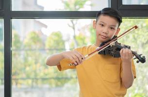 een klein Aziatisch kind speelt en oefent viool muzikaal snaarinstrument tegen in huis, concept van muzikaal onderwijs, inspiratie, tiener kunstacademie student. foto