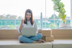 gelukkige jonge aziatische vrouwelijke ondernemer, glimlach voor verkoopsucces na het controleren van de bestelling van de online winkel in een laptop thuiskantoor, concept van online handelszaken en e-commerce foto