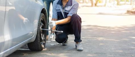 expertise monteur man in uniform die kracht gebruikt om de wielbouten los te draaien en een vrouw te helpen bij het verwisselen van het autowiel op de snelweg, autoservice, reparatie, onderhoudsconcept. foto