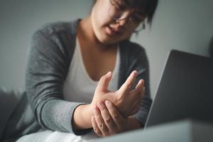 vrouw die haar handpijn vasthoudt van het lange tijd gebruik van de computer. kantoor syndroom concept. foto