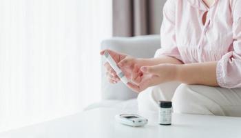 Aziatische vrouw die lancet op vinger gebruikt voor het controleren van de bloedsuikerspiegel door glucosemeter, gezondheidszorg en medisch, diabetes, glycemieconcept foto