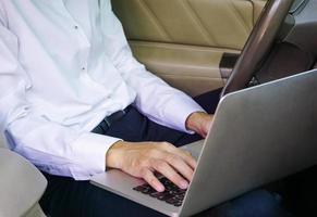 zakenman die op laptop werkt terwijl hij op de bestuurdersstoel in de auto zit. levensstijl concept. foto