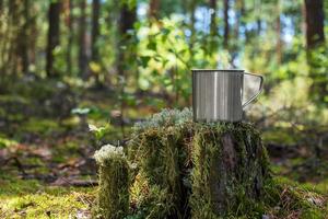 metalen toeristische mok met warme drank staat op stronk in het bos. foto