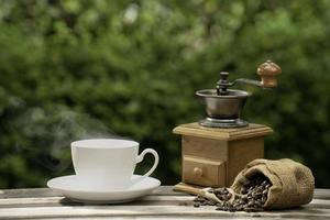 koffiekopje met een molen, donkere koffiebonen op de oude houten vloer, close-up van koffiezaden op een natuurlijke achtergrond. foto