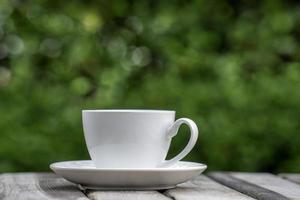 warme koffie drinken concept, hete keramische witte koffiekopje met rook op een oude houten tafel in een natuurlijke achtergrond. foto