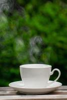 warme koffie drinken concept, hete keramische witte koffiekopje met rook op een oude houten tafel in een natuurlijke achtergrond. foto