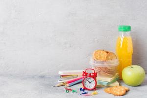 schoolbenodigdheden en ontbijtcrackers, sinaasappelsap en verse appel op de grijze tafel met kopieerruimte. conceptschool. foto