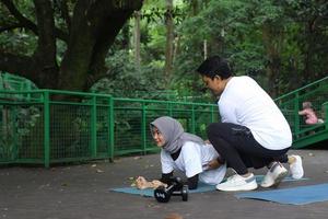 jonge aziatische man die zijn vrouw helpt met het doen van plank op yogamat in het park. gezonde levensstijl paar concept. foto