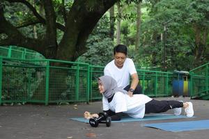 jonge aziatische man helpt zijn vrouw plank te doen in het park. gezonde levensstijl paar concept. foto