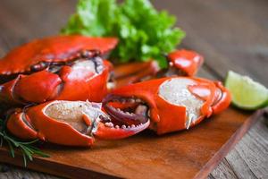verse krab op houten plaat, gekookte of gestoomde krab rood in het restaurant, klauw krab koken voedsel zeevruchten plaat met chili kruiden specerijen citroen limoen salade foto