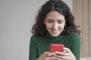 zelfverzekerde lachende Spaanse zakenvrouw die mobiele telefoon gebruikt terwijl ze thuis aan een bureau zit foto