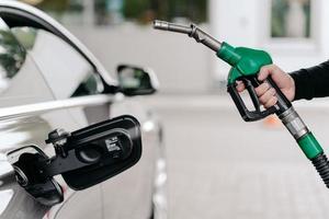 bijgesneden opname van de hand van de man die benzine in de auto pompt bij het benzinestation. auto wordt gevuld met benzine. onherkenbare man houdt brandstofnozzel vast. foto