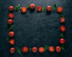 plat leggen van rode rijpe tomaten ligt in de vorm van een frame op een donkere achtergrond met groene peterselie en dille. gezond vegetarisch gerecht. horizontaal schot. kopieer ruimte voor tekst foto