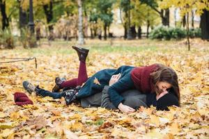 vriend en vriendin hebben een romantische kus terwijl ze op gele bladeren in het park liggen, zonnige herfstweekenden samen doorbrengen, een goed humeur hebben. verliefde paar genieten van saamhorigheid buitenshuis. seizoen en mensen foto
