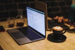 een mok 3d latte art-koffie in de vorm van een schattige kat met een laptop op de achtergrond. foto