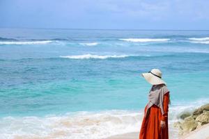 moslimvrouwenreiziger in oranje jurk met hoed loopt een wandeling op zomervakantie op het perfecte witte zandstrand foto