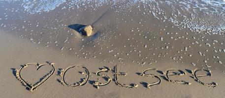 het Duitse woord Oostzee Oostzee en een hart geschreven in het zand van het strand. foto