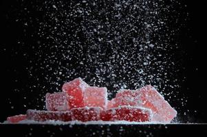 poedersuiker wordt gestrooid op bessenmarmelade op een zwarte achtergrond. aardbei rode marmelade jelly candy's bedekt met poedersuiker op zwarte achtergrond. foto met kopie ruimte.