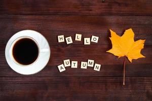 hallo herfstconcept. kopje koffie en gevallen bladeren op bruin houten achtergrond. warme drank voor koud weer. foto