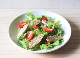 tempeh of tempe salade met tomaat en groene groente in witte plaat op houten tafel. foto