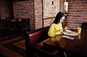 grappige brunette meisje in gele trui pizza eten in restaurant. foto