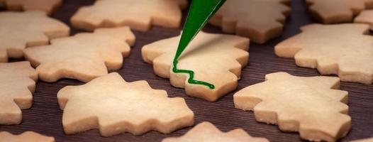 close-up van het tekenen van kerstboom suiker cookie op houten tafel achtergrond met slagroom. foto