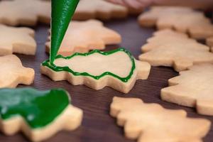 close-up van het tekenen van kerstboom suiker cookie op houten tafel achtergrond met slagroom. foto